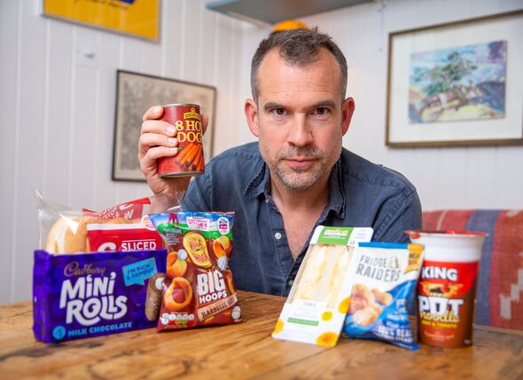 Dr Chris van Tulleken sits at a table with lots of ultra processed foods