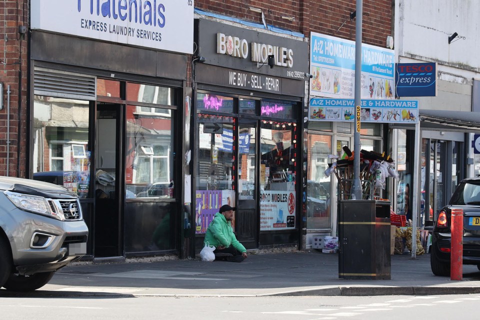 Person sitting on the sidewalk outside of shops.