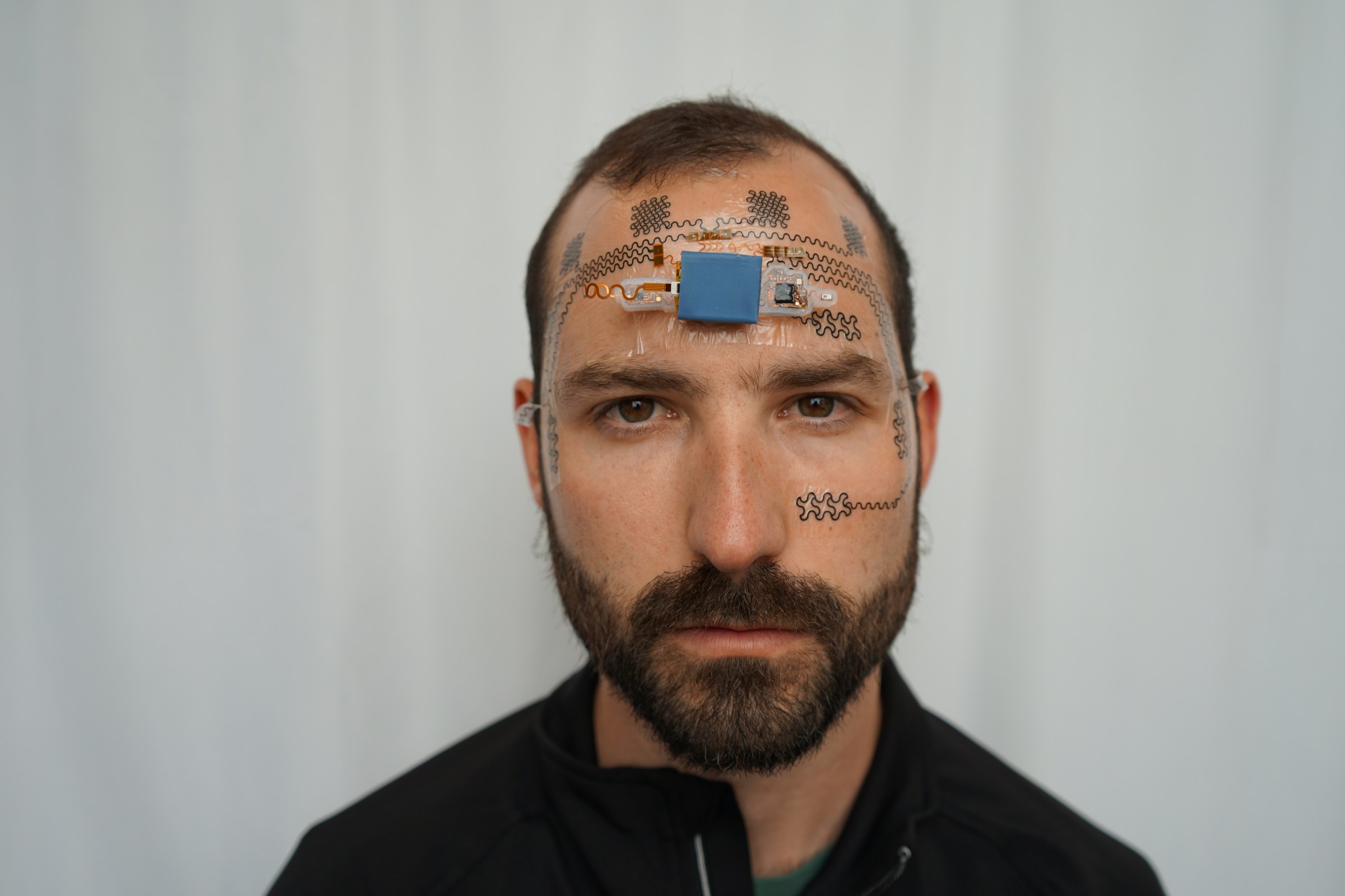 Front on view of man staring straight forward while wearing electrodes on his forehead and face