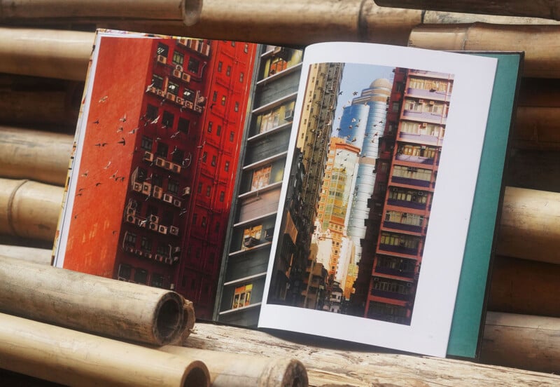 An open book resting on bamboo poles displays colorful photographs of tall, closely packed urban buildings with numerous windows and balconies.