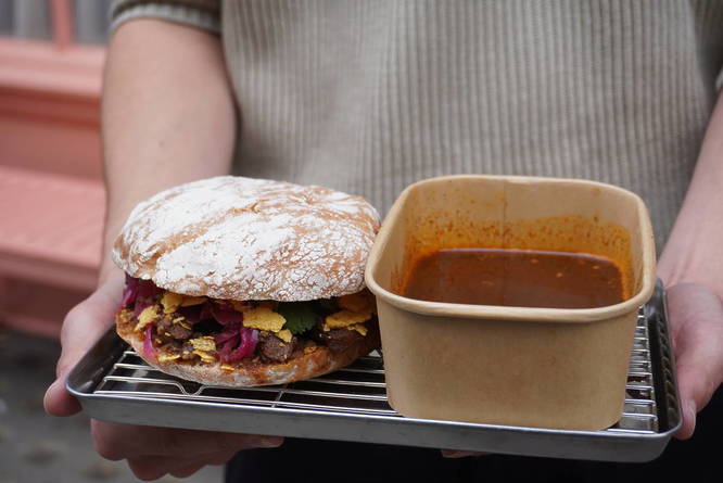 Someone holding a tray with a sandwich next to a pot of dipping sauce on it