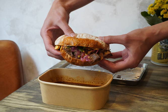 The Secret London sandwich being held up, drenched in birria dipping sauce