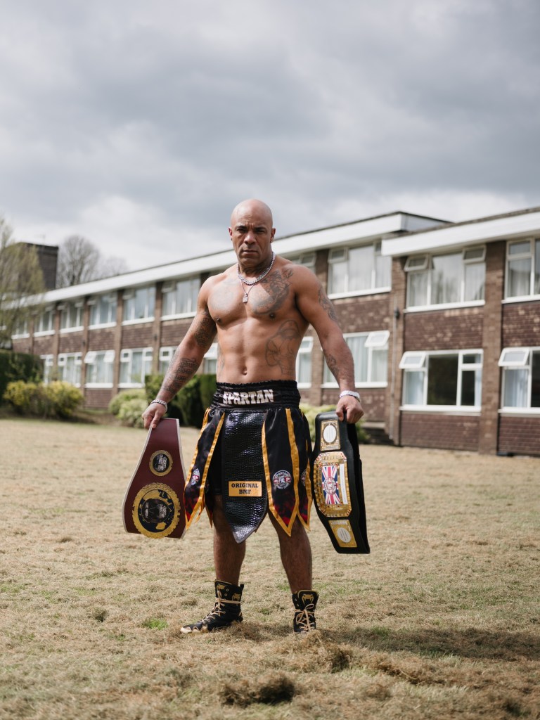 A fighter poses outside houses with his winning belts