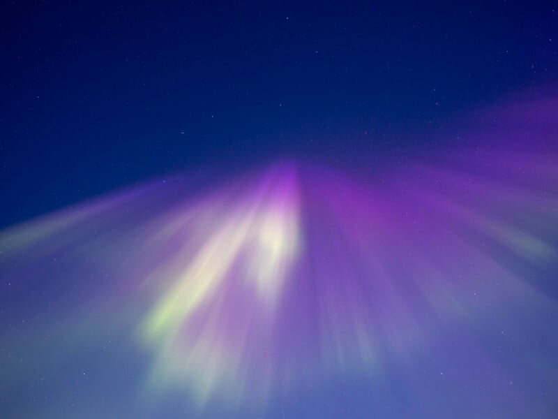 Colorful aurora lights in shades of purple, pink, and green spread across a dark night sky with faint stars visible in the background.