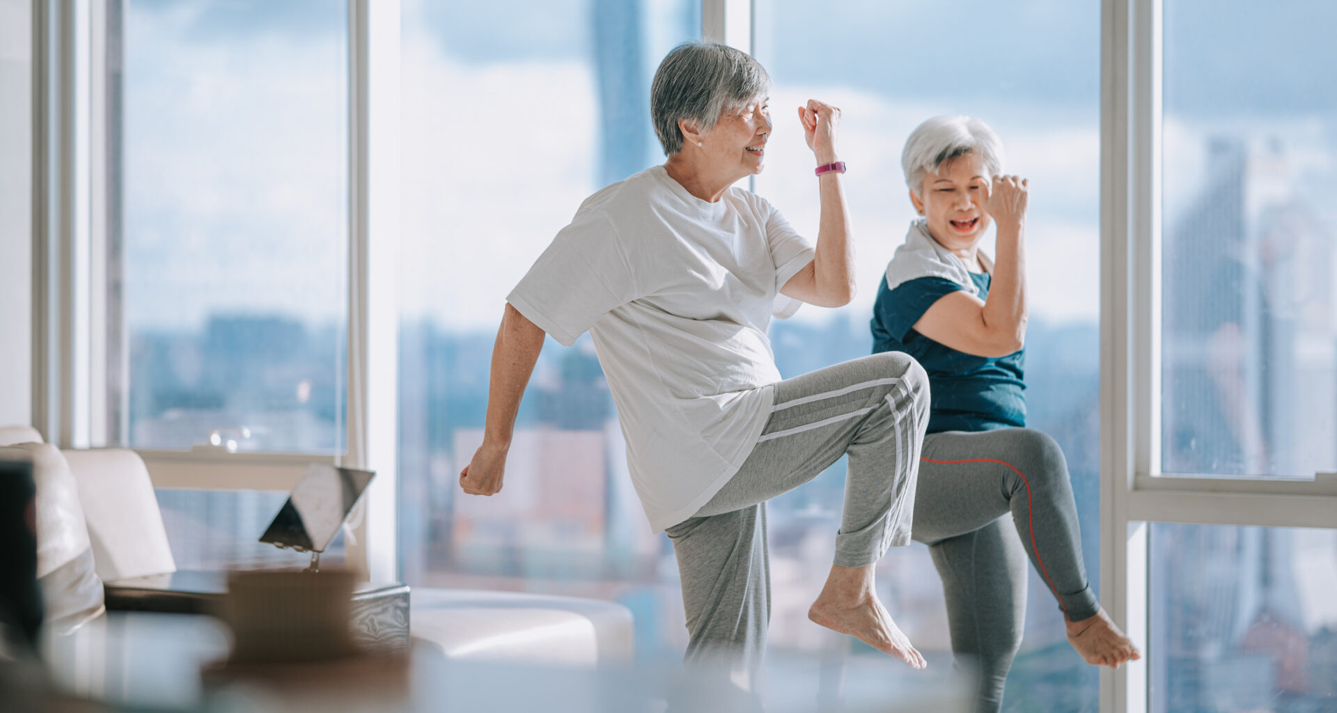 Two women in a domestic setting exercising, with one knee raised in the air.