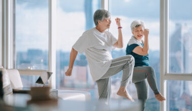 Two women in a domestic setting exercising, with one knee raised in the air.