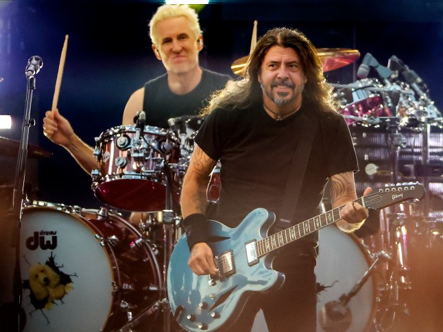 Dave Grohl and Josh Freese of Foo Fighters performing onstage. Dave is playing a guitar while John is playing drums. They are both wearing black outfits