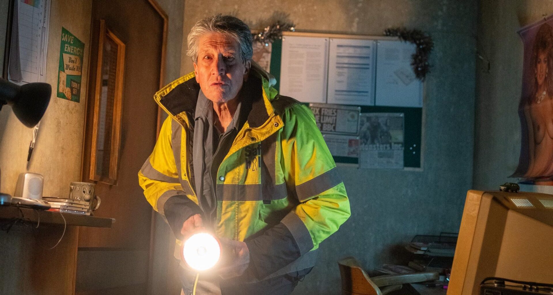 A man in a yellow high vis jacket shining a torch in a small room.