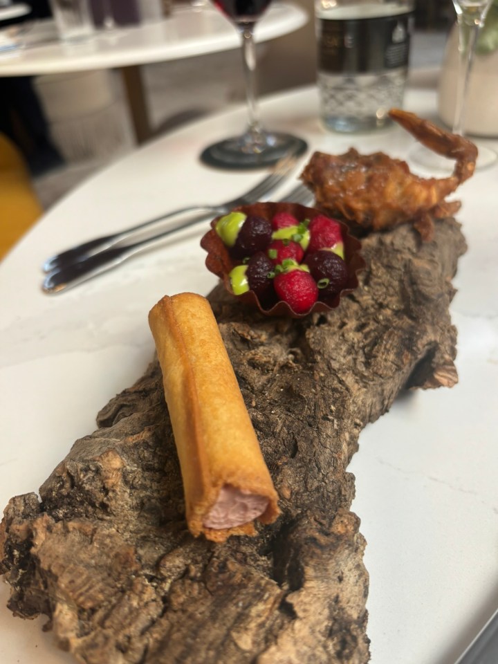 Appetizer platter with fried crab, fruit salad, and pastry on a wood slice.