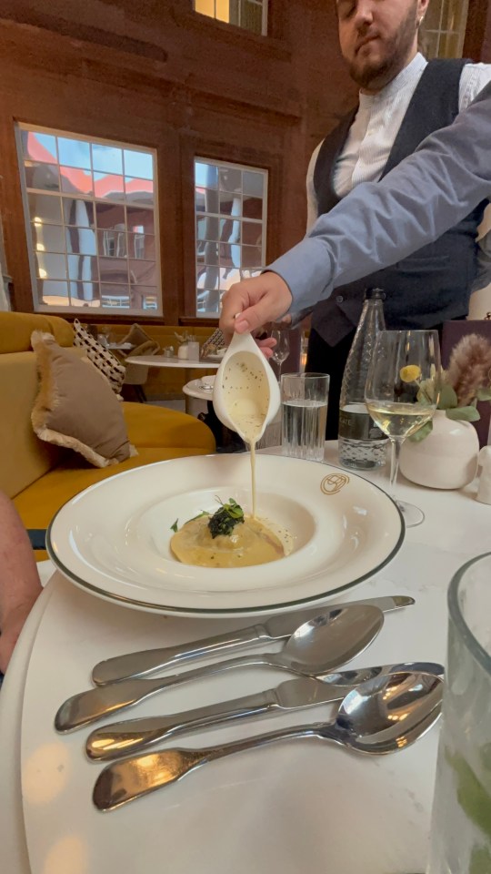 Waiter pouring sauce over pasta dish.