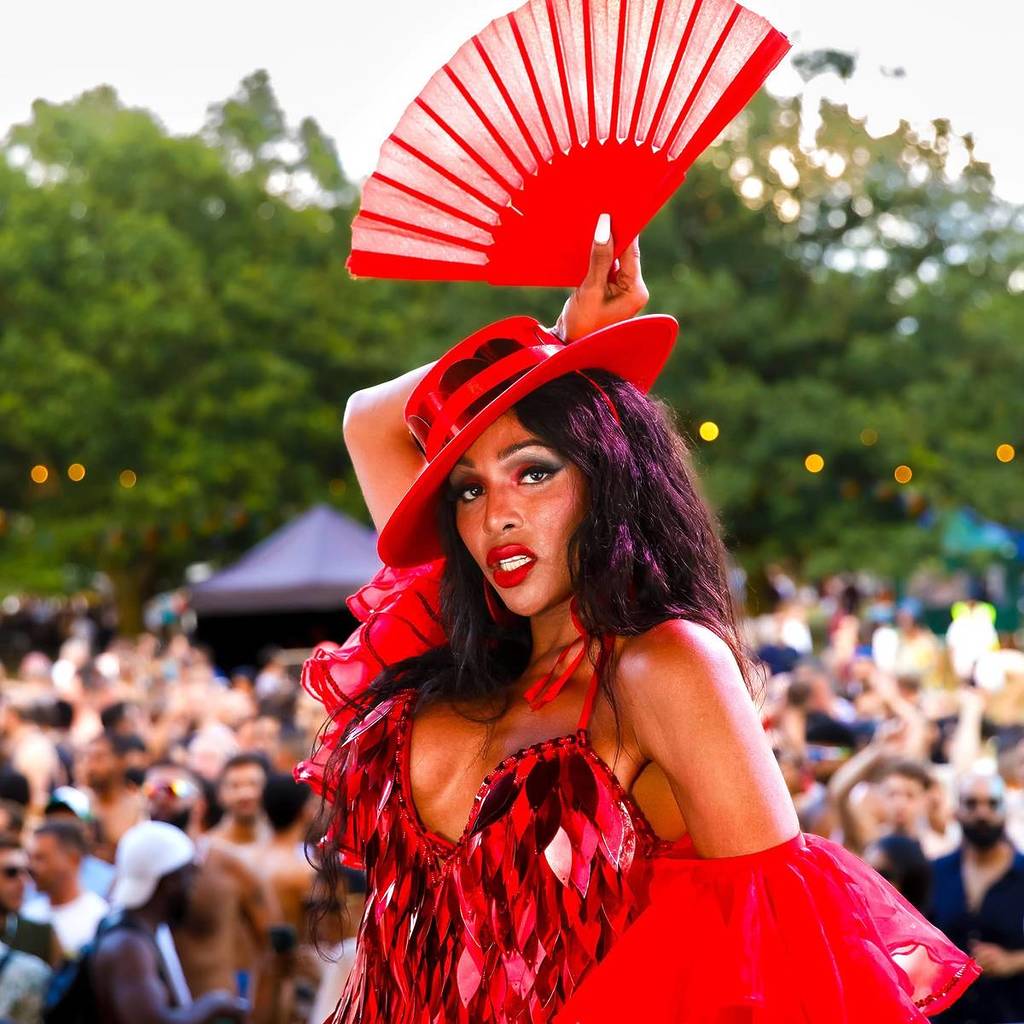 A drag queen performs in a fabulous, red cheeky outfit in front of a crowd; she is in-focus, they're blurred.
