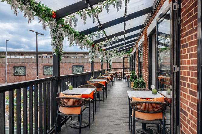 An outdoor bar terrace with tables and chairs and hanging plants festooned above