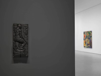A bronze work resembling a carving of a man seen from behind mounted to a grey wall.
