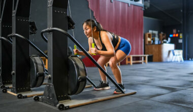 Woman using cardio machine in the gym. She is holding two green handles connected to cords and is bent over