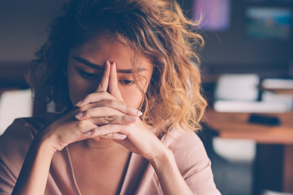 Sad young woman sitting at a cafe, head in hands.