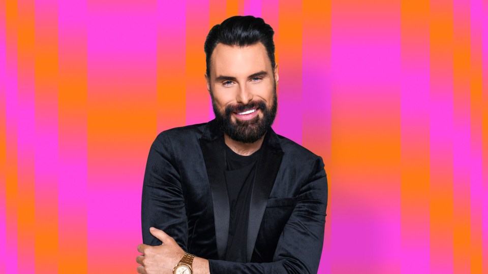 Rylan, smiling, in a black velvet jacket.