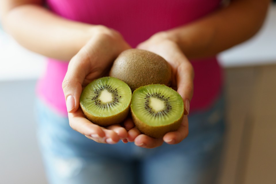 Woman holding two kiwi fruit halves and one whole kiwi.
