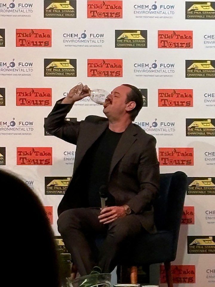 Man in suit drinking wine while seated.