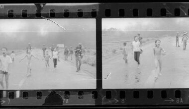 Black and white film negatives show children and soldiers running on a road; smoke rises in the background. One child in the foreground appears distressed and unclothed. The scene is tense and chaotic.