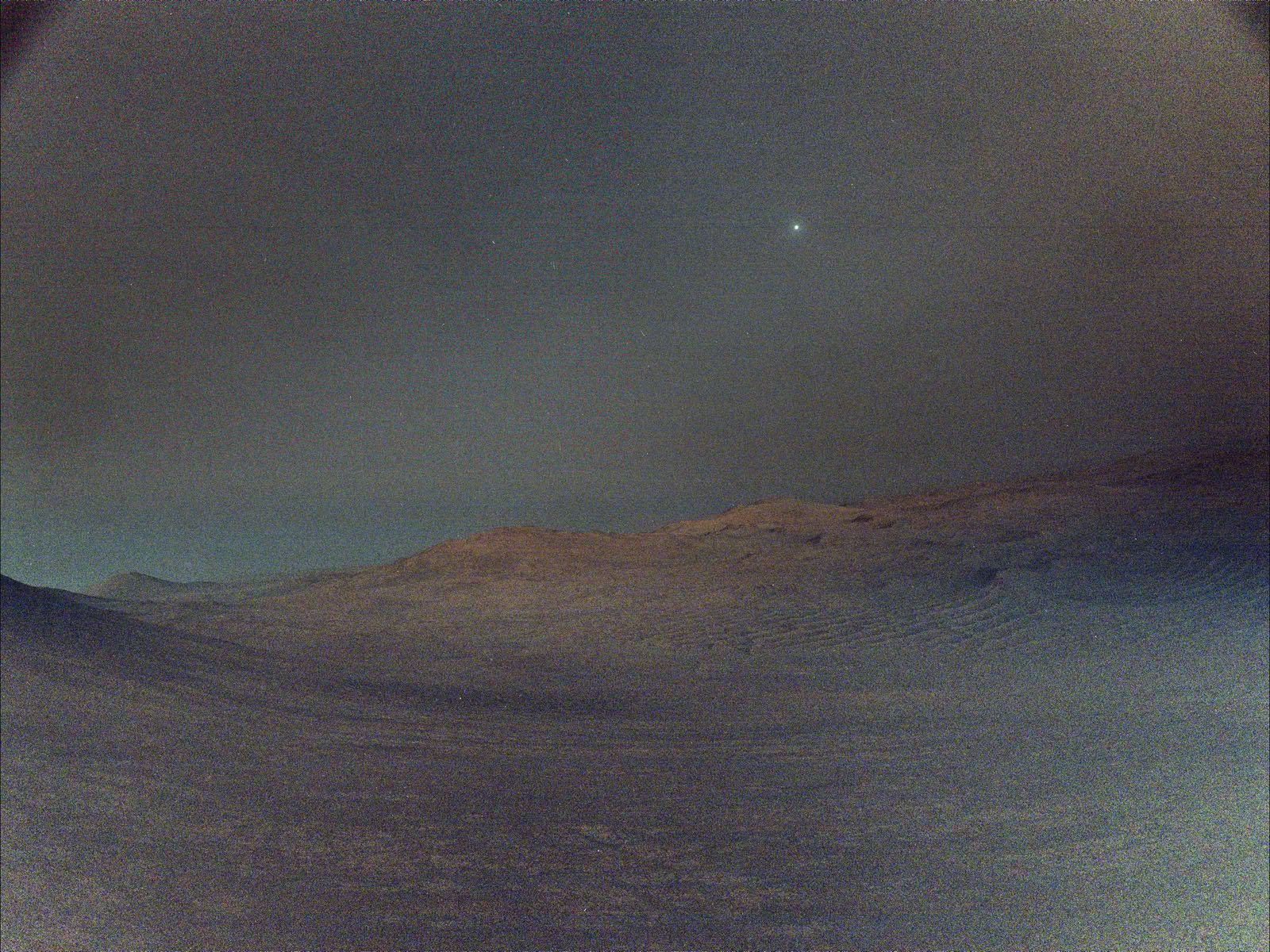 A dusty, barren Martian landscape under a hazy sky, with a single bright star or planet shining above rocky hills on the horizon.