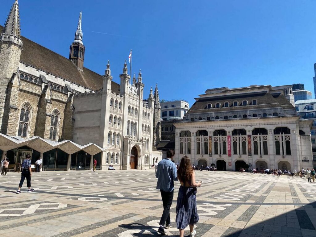 two figures cross a sunny courtyard outside Guildhall Art Gallery
