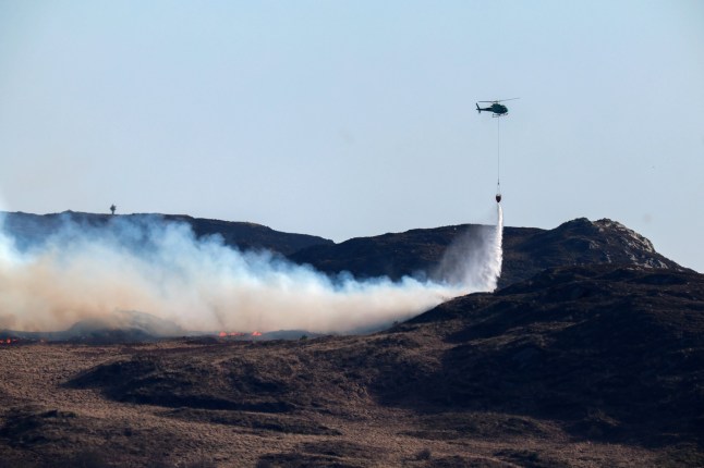 COLINTRAIVE, SCOTLAND - APRIL 10: A helicopter douses a wild fire with water on the Isle of Bute on April 10, 2025 in Colintraive, Scotland. There has been a rise in the number of wildfires across the UK this year, which reports say, although this March was the fourth driest on record, are as much attributable to human intervention as climate. (Photo by Jeff J Mitchell/Getty Images)