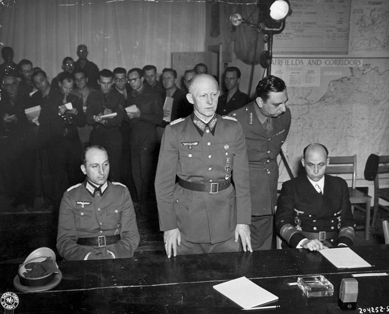 (Original Caption) 5/6/1945-Rheims, France: World War II defeat. The Nazi Chief of Staff, Col. Gen. Gustaf Jodl, stands at table in war room of SHAEF headquarters at Rheims, France, ready to sign unconditional surrender terms. With him are Maj. Wilhelm Xeniue, an aide, left, and Gen. Adm. Hans George Von Friedburg, Commander-in-Chief of the German fleet.