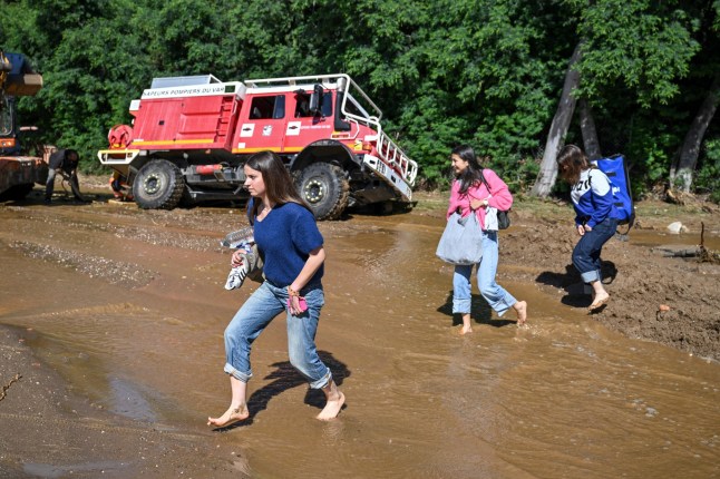 TOPSHOT - People walk through the water to cross amud-covered road as a firefighting vehicle gets stuck in the mud following a flood caused by heavy rain in Cavaliere village of Le Lavandou commune in the Var department, southeastern France, on May 20, 2025. Intense rainstorms in the southeastern Var department have left at least three people dead, including an octogenarian couple in Le Lavandou, on the coast, authorities reported. (Photo by Christophe Simon / AFP) (Photo by CHRISTOPHE SIMON/AFP via Getty Images)