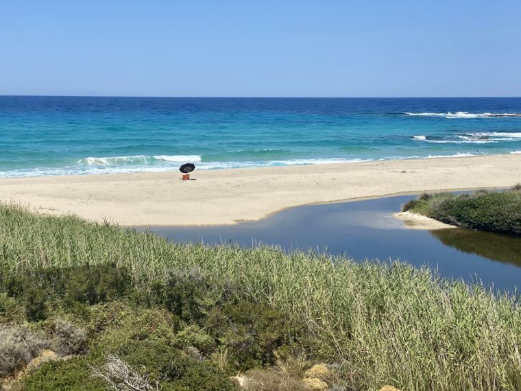 Two sunlounges with a sun umbrella in an empty beach in Ikaria, an island in Greece