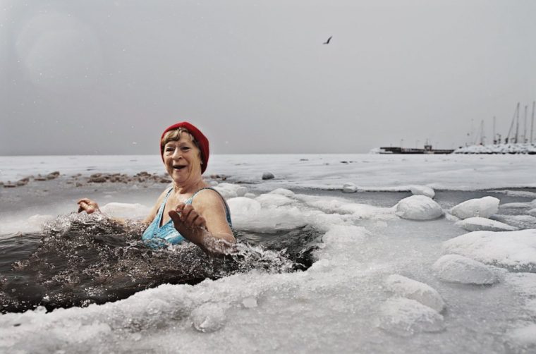 Woman wearing red beanie bathing in a hole in the ice in the frozen sea.