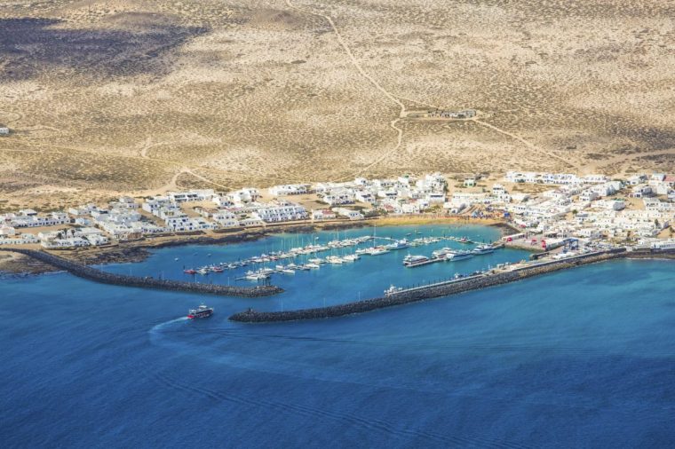 View over the village of Caleta del Sebo, La Graciosa, from the Mirador del Rio, inter-island ferry entering the harbour, Ye, Haria, Lanzarote, Las Palmas, Islas Canarias, Spain, Europe. The Mirador del Rio clifftop viewpoint clings to the edge of the Risco de Famara 1500 feet above sea level and affords fine views over the island of La Graciosa and El Rio, the strait which separates it from Lanzarote. There is a regular ferry service between Orzola and Caleta del Sebo, La Graciosa's main settlement.