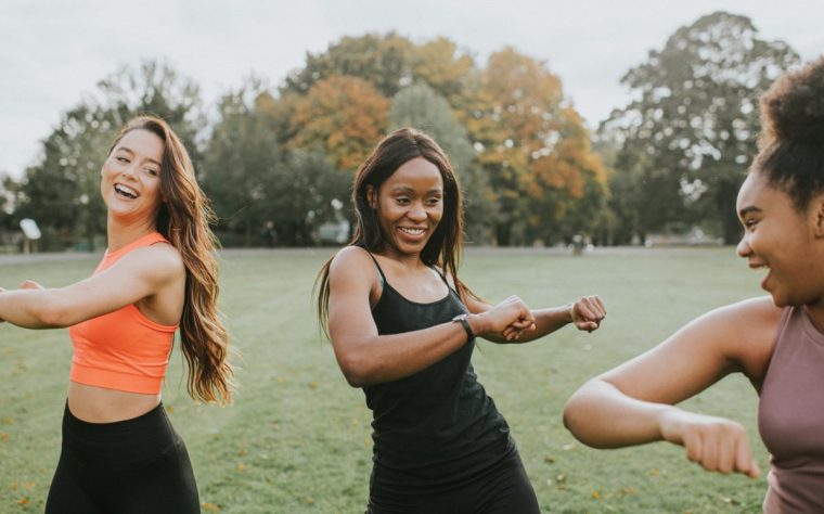 Woman warming up before sports training together. They stretch out their back and hip muscles while having a lighthearted conversation with each other.