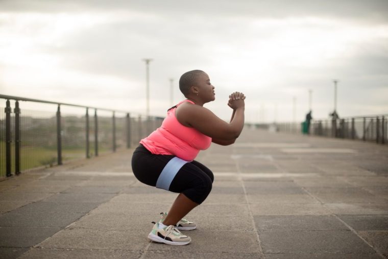 Plus size, fitness and black woman squat outdoor for wellness, training or cardio exercise. Weight loss, sports or profile of African female person on a sidewalk for body workout, health or challenge