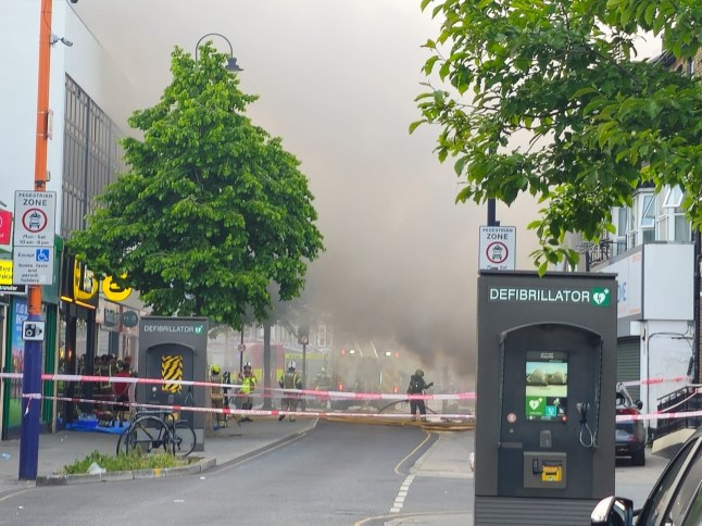 A significant fire has broken out at a shop with residential flats above on High Street North, East Ham, with ten fire engines and approximately 70 firefighters battling the blaze this evening, Thursday 29 May 2025. The fire was first reported to London Fire Brigade (LFB) at 19:02, when Control Officers received the first of 12 emergency calls reporting smoke and flames emerging from a mid-terraced commercial property. Blaze Declared Major Incident Firefighters arriving from East Ham, Plaistow, Stratford, and surrounding fire stations found half of the ground floor shop unit alight, with fears the fire could spread to the dwellings located on the floors above. A major incident has been declared by the Met Police as crews work swiftly to contain the flames and prevent further escalation. What We Know So Far: Location: High Street North, East Ham, E6 Time of first call: 19:02 BST Response: 10 fire engines, approx. 70 firefighters Involved structure: Shop with residential flats above Fire status: Half of shop alight, crews actively tackling blaze Injuries: No confirmed casualties at this time Public Advice Authorities are urging people to avoid the area and keep windows and doors shut due to thick smoke affecting surrounding streets. High Street North remains partially closed, with diversions in place. The incident is likely to cause significant travel disruption this evening. London Fire Brigade Statement An LFB spokesperson said: ???Crews are working in challenging conditions to bring the fire under control. Our firefighters are using breathing apparatus, hose reels and main jets to tackle the flames and protect adjacent properties.???