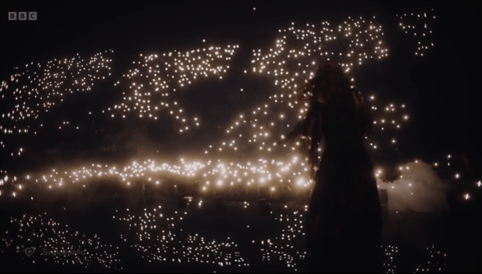 Silhouette of a person performing on stage surrounded by a crowd holding up lights.