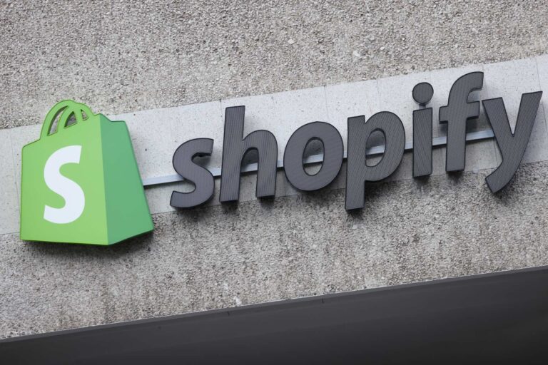 A sign with the Shopify logo, a green bag with an "S" on it, and the text Shopify on a concrete building wall