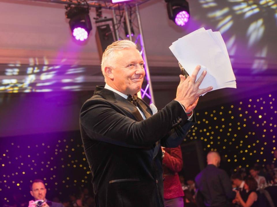 Man in tuxedo holding papers on stage.