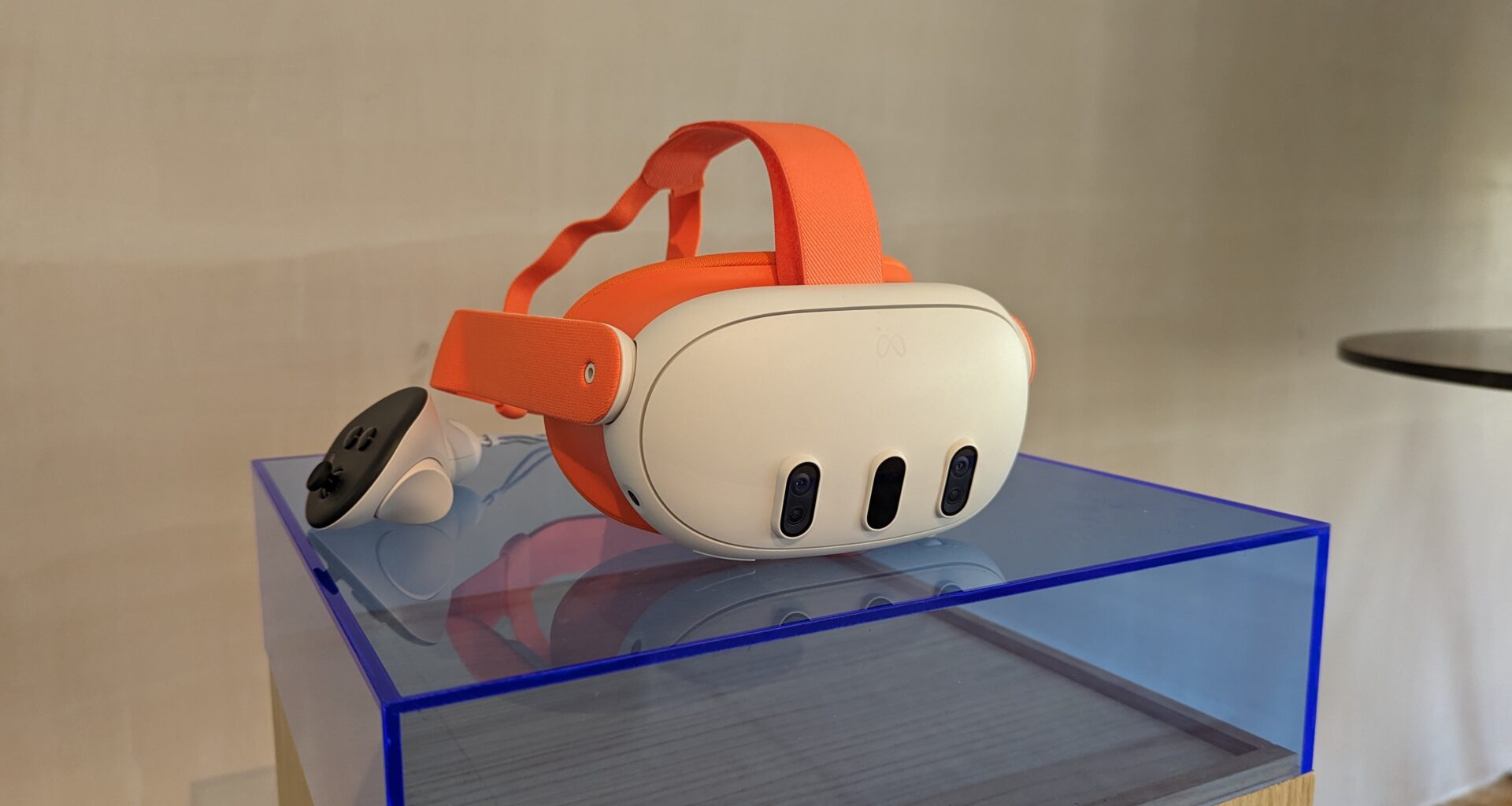 An orange Meta Quest 3 and its controllers on a blue plastic plinth in front of a blank wall