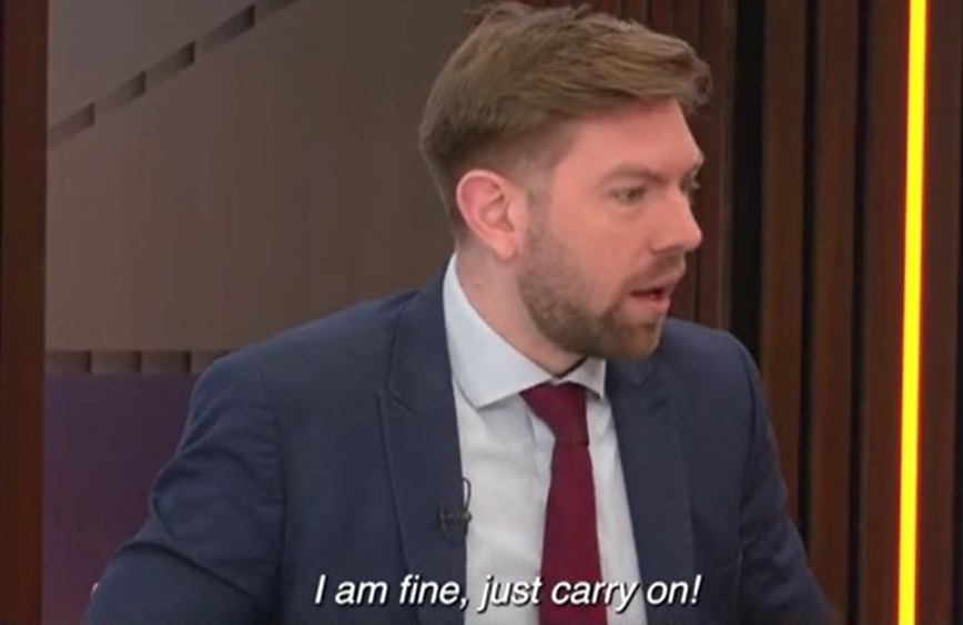 Man in suit says, "I am fine, just carry on!"