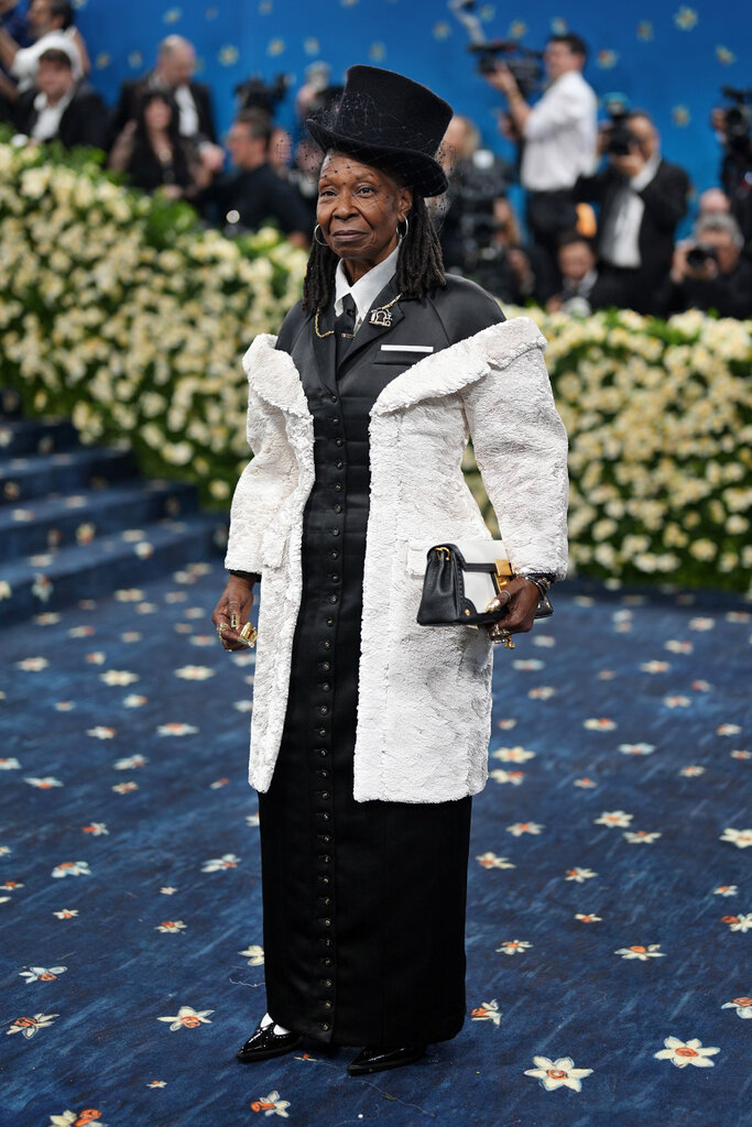 Whoopi Goldberg in a long black dress with buttons in the front with an attached furry, white coat.
