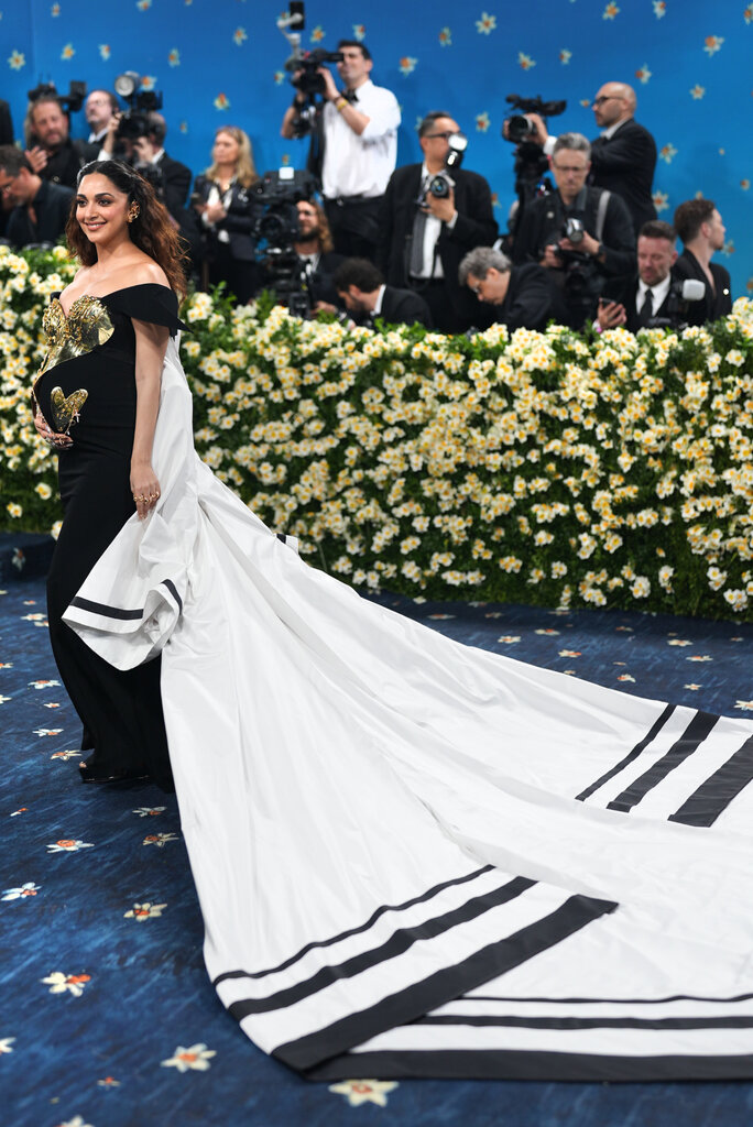 Kiara Advani is wearing a black gown with a gold sequined bodice and a long white train with black striped trim.