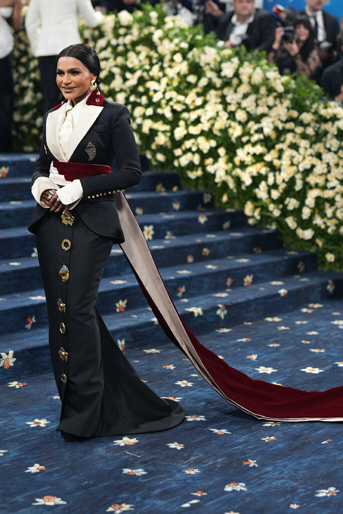 Mindy Kaling wearing a navy blue dress with a matching blazer and long red belt. 