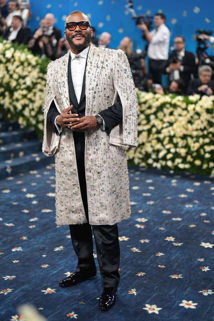 Tyler Perry wearing a black suit and long, cream jacket with jewels.