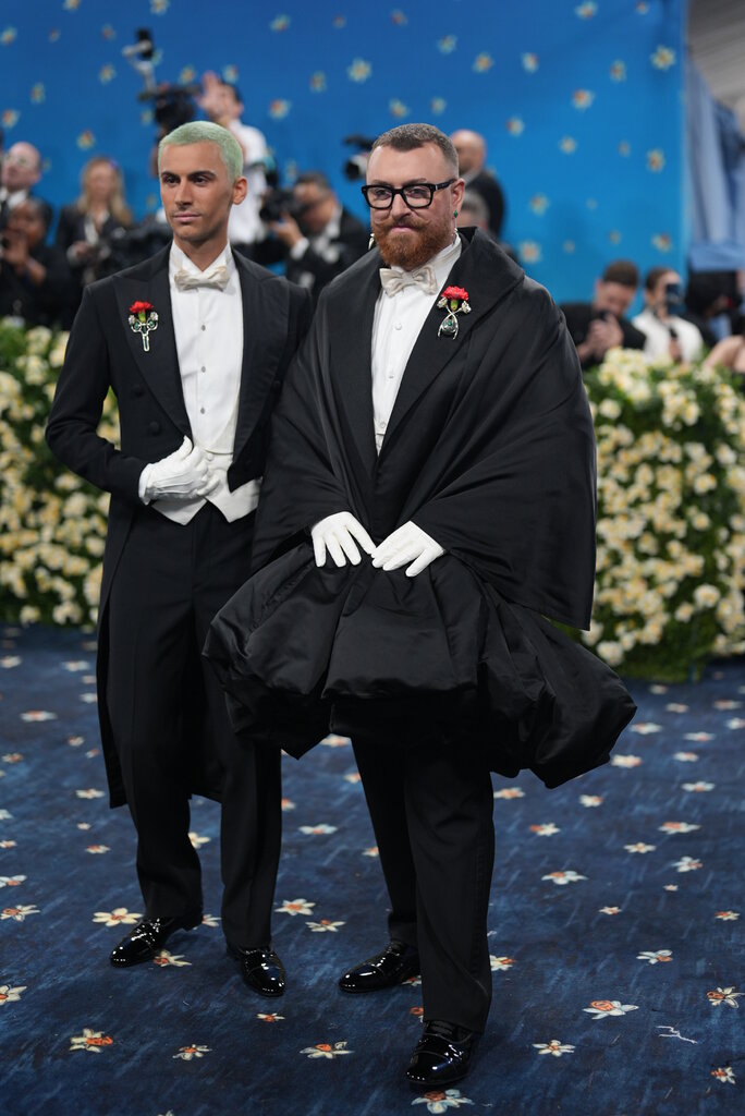 Christian Cowan and Sam Smith, both wearing black suits and white gloves. Sam Smith's suit is made from a puffy, coat material.