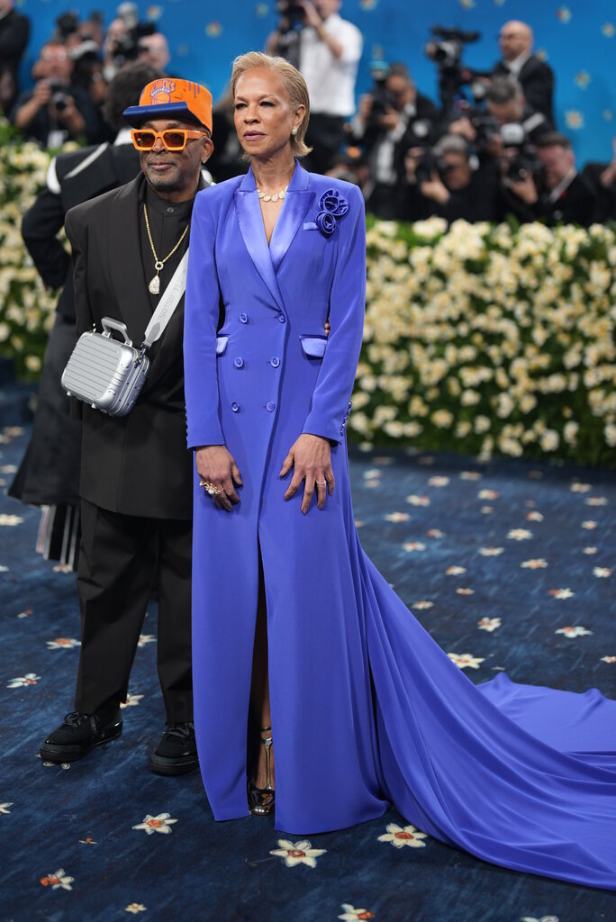 Spike Lee is wearing a black suit and orange and blue hat with matching sunglasses. Tonya Lewis Lee is wearing a blue gown that resembles a suit blazer.