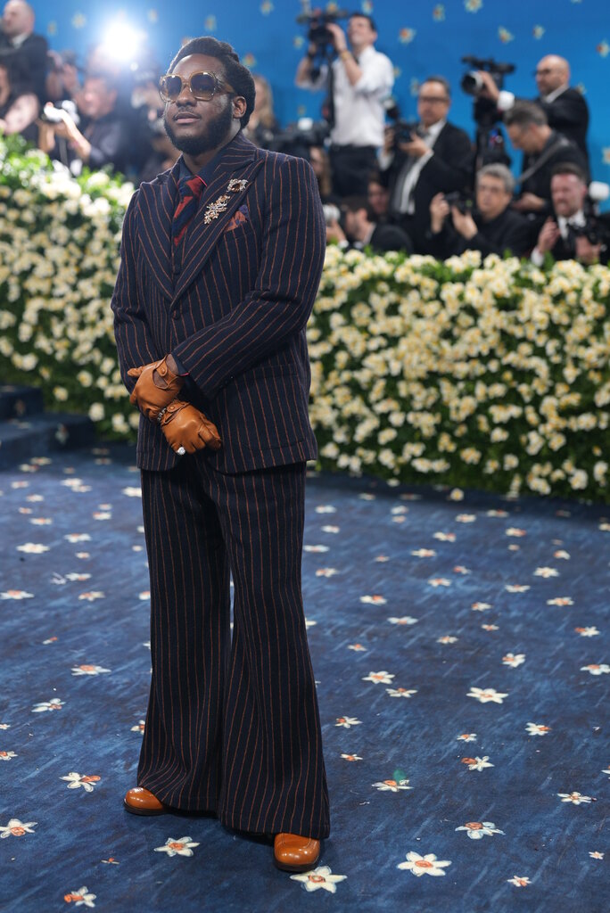 Leon Bridges is wearing a blue pinstripe suit and tan leather gloves.