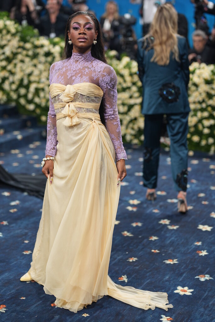 Sha’Carri Richardson wearing a purple see-through turtleneck under a yellow dress. 