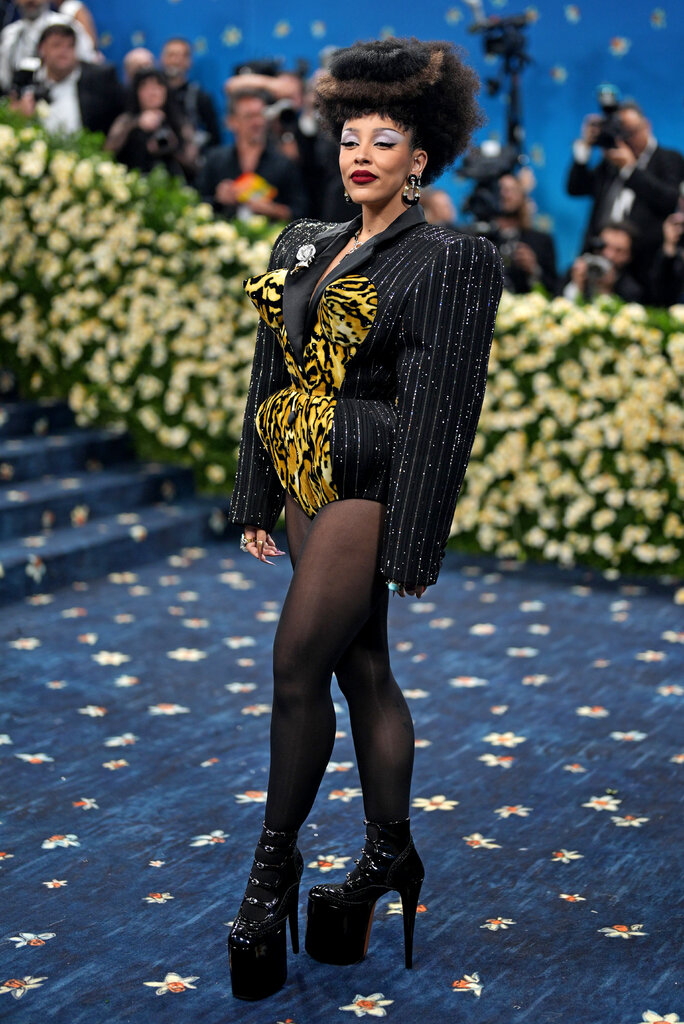 Doja Cat wearing a jeweled pinstripe bodysuit with exaggerated shoulders, a pointed cone bust line and animal print detail along the front, overtop black tights and platform heels.