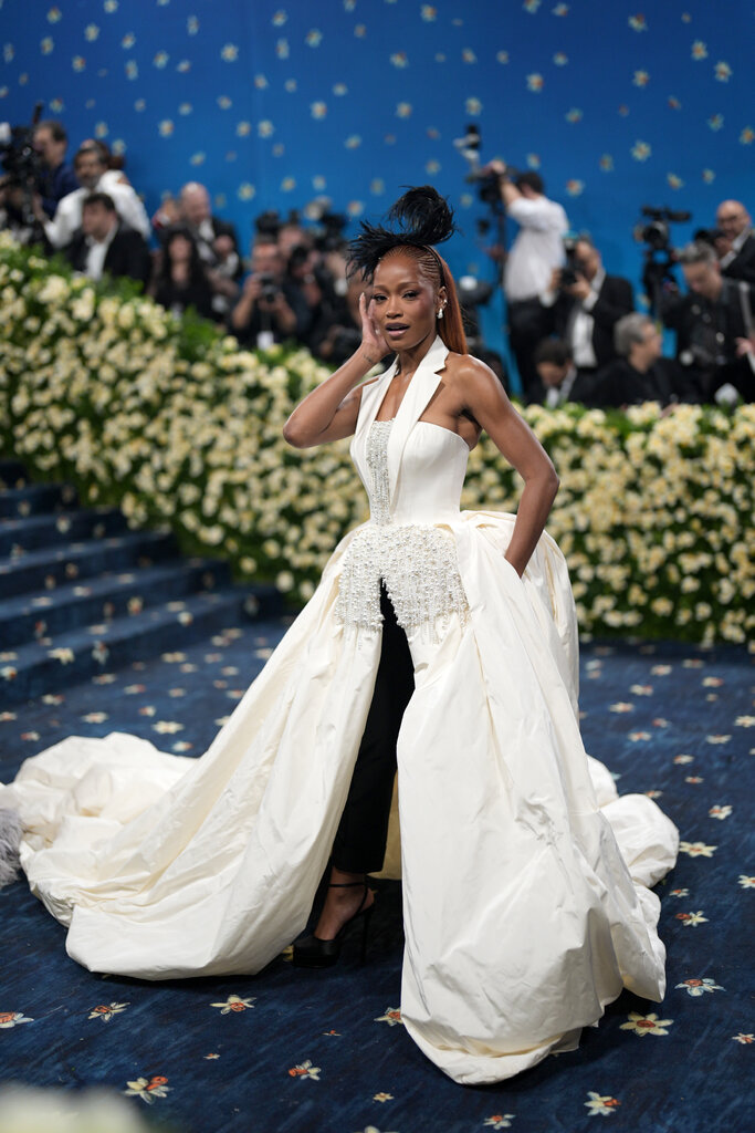 Keke Palmer wearing a black, feathered hat and a cream dress with a poofy skirt. 
