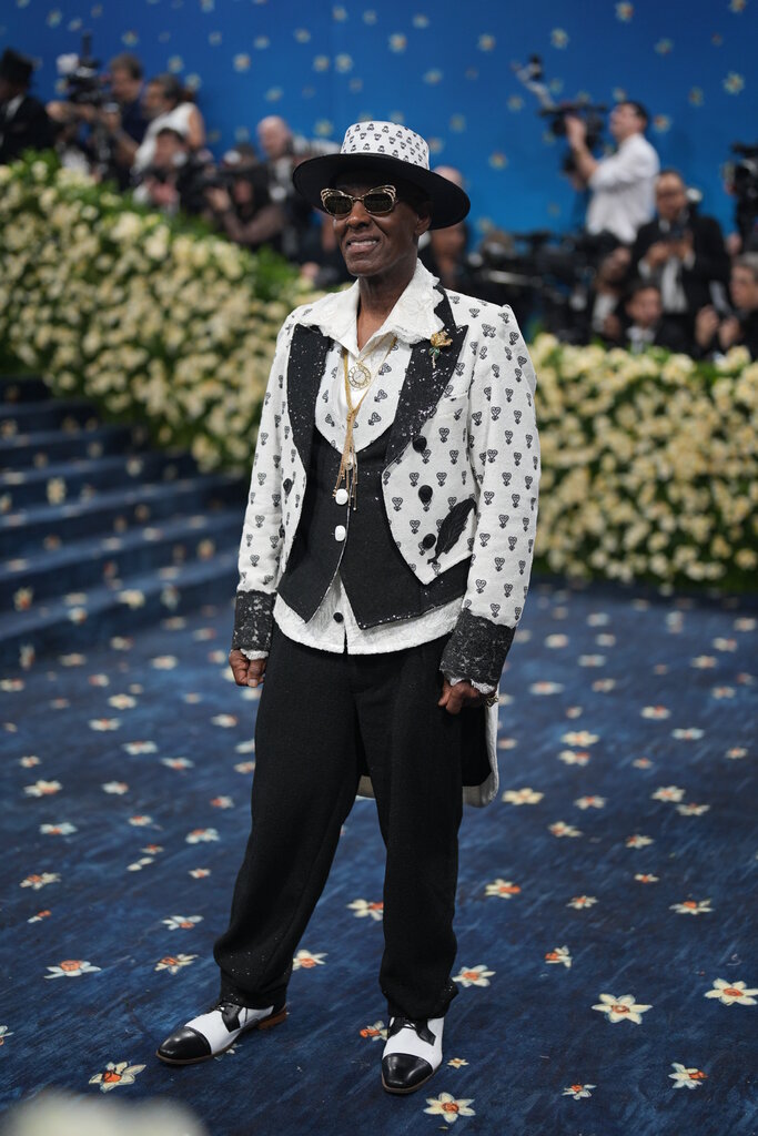 Dapper Dan wearing a black and white tuxedo jacket with black trousers, sunglasses with curved frames and a flat-brim hat.